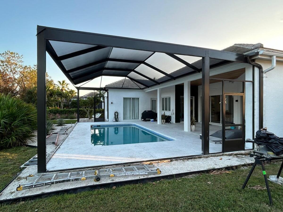 A Marblu screen enclosure structure under construction beside a Florida pool, showing the engineering before the finish