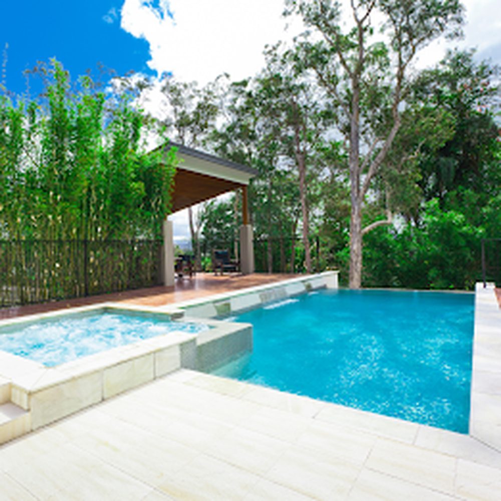 Pool and integrated spa surrounded by light stone deck and covered lounge area