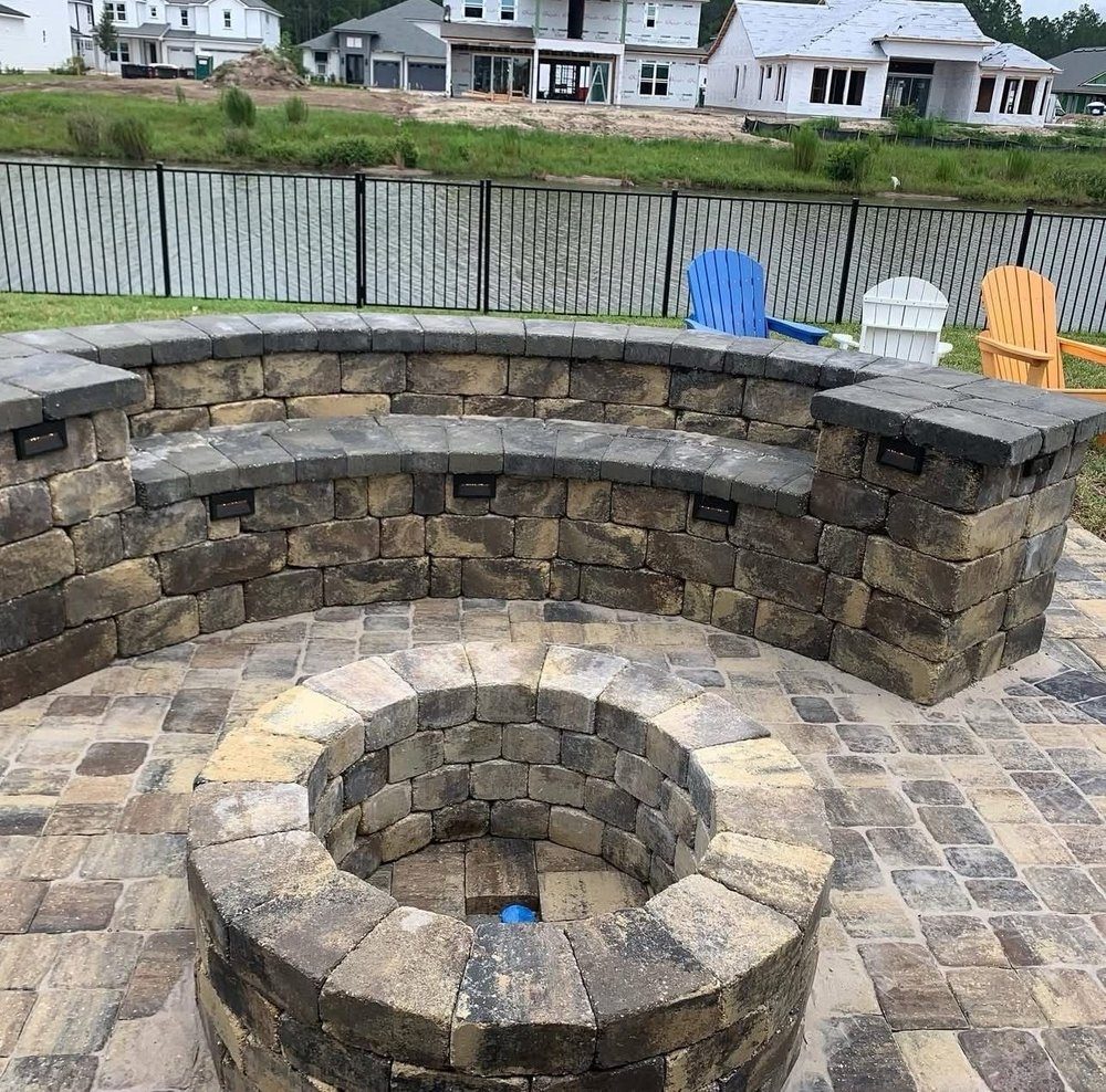 Stone seating wall wrapping a masonry fire pit on a paver terrace by the lake