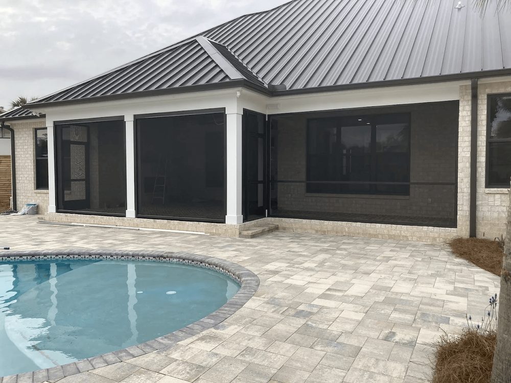 Pool and light stone deck beside a screened Florida home, built by Marblu