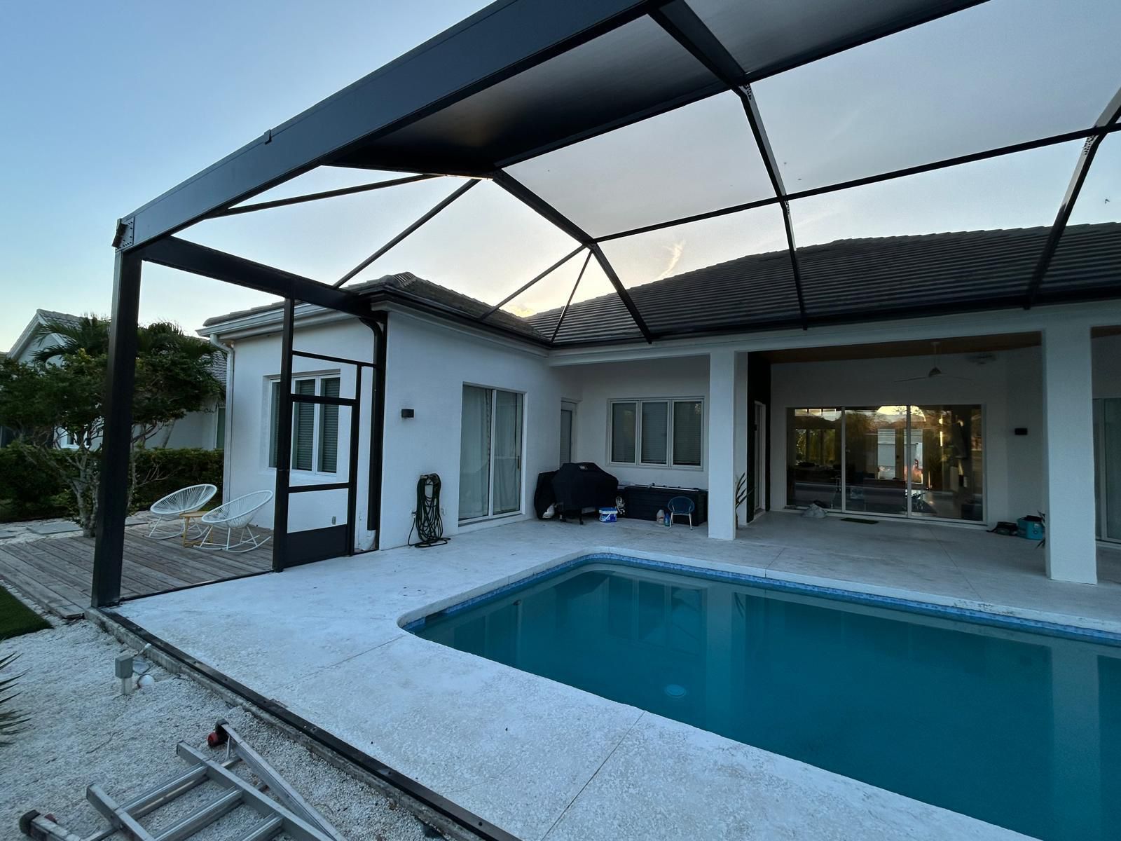 Contemporary black-frame screen enclosure over a travertine pool deck at dusk, Jacksonville