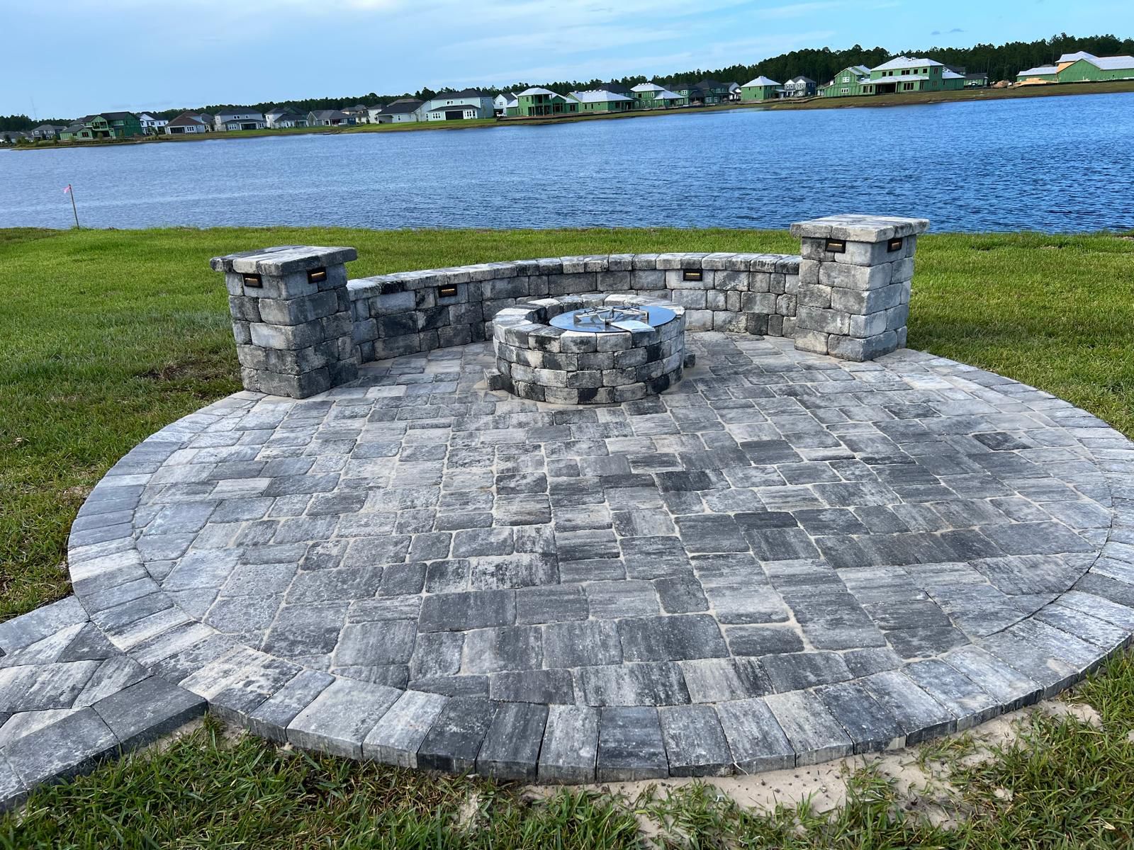 Circular paver terrace with masonry fire pit and curved seating wall overlooking the lake