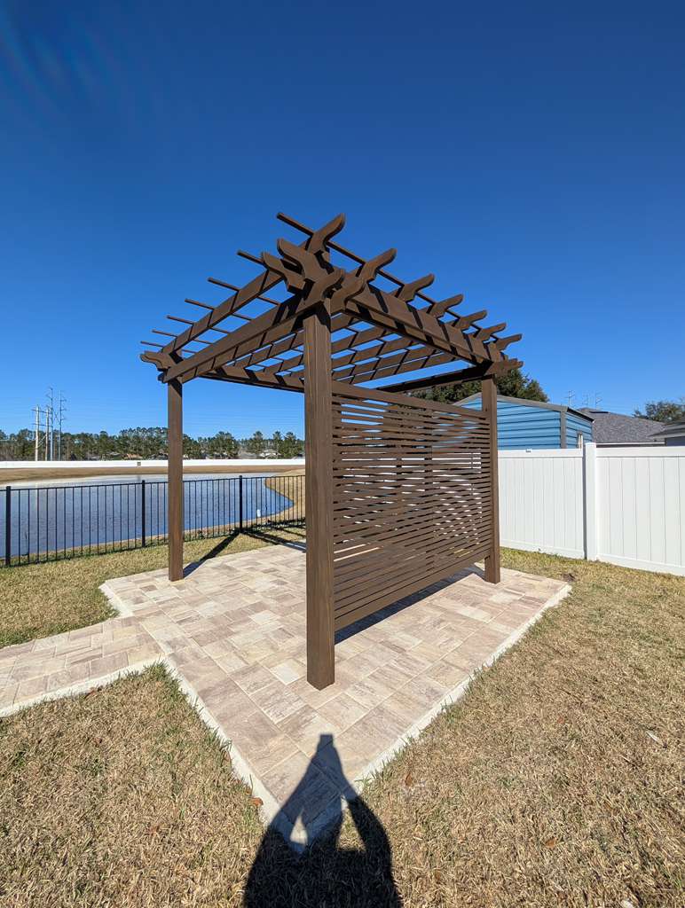 Freestanding pergola with privacy screen over a paver base beside a lake