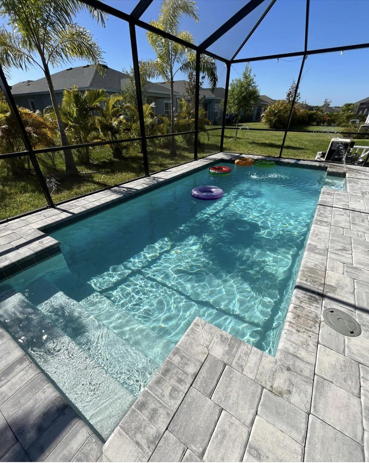 Grey paver pool deck inside a screen enclosure with float rings in the water