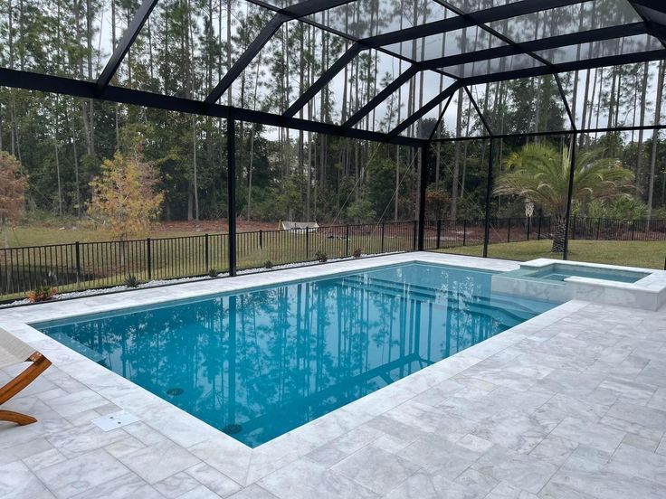 Pool with white travertine deck and black screen enclosure framing the trees