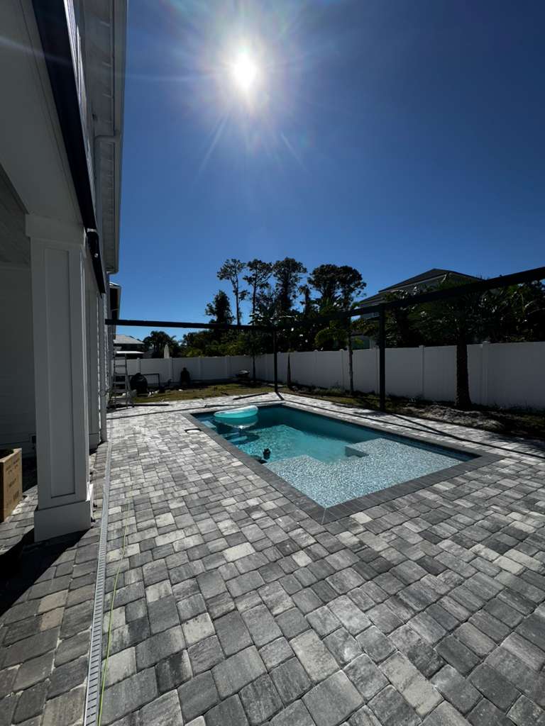 Grey paver pool deck under intense Florida sun with enclosure framing in progress